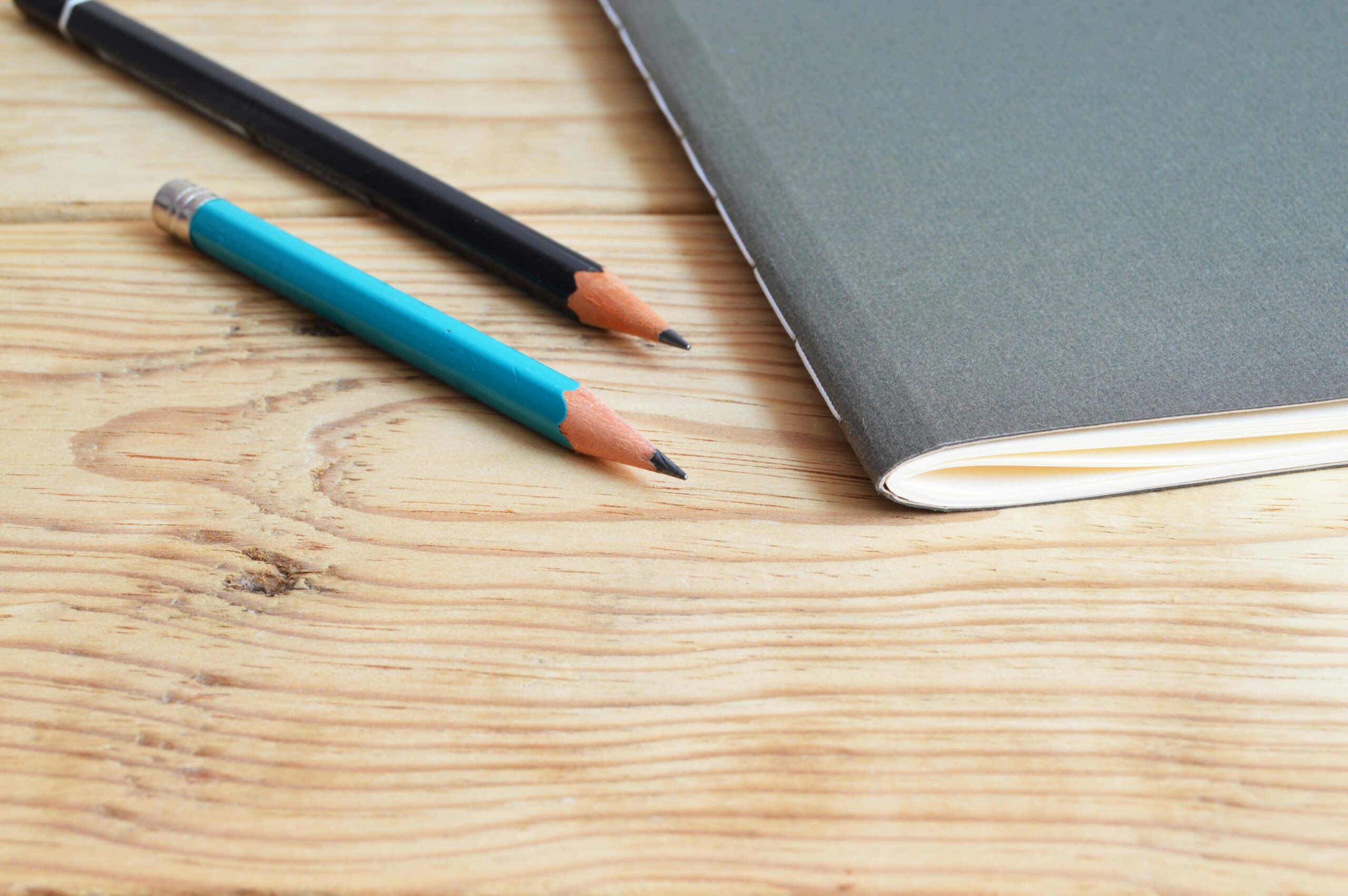 A minimalist composition of a notebook and pencils on a wooden desk, ideal for study themes.